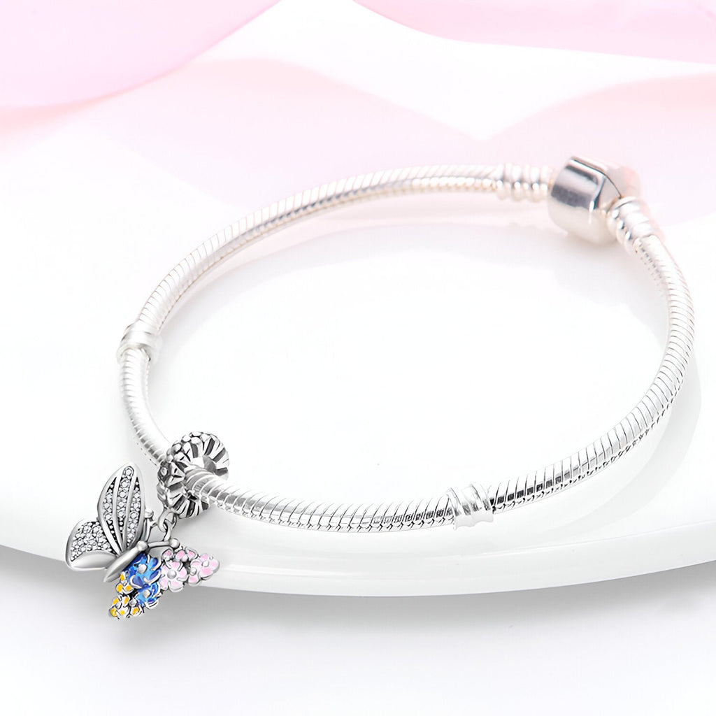 Bracelet argenté avec pendentif papillon aux ailes décorées de fleurs colorées bleu et rose.