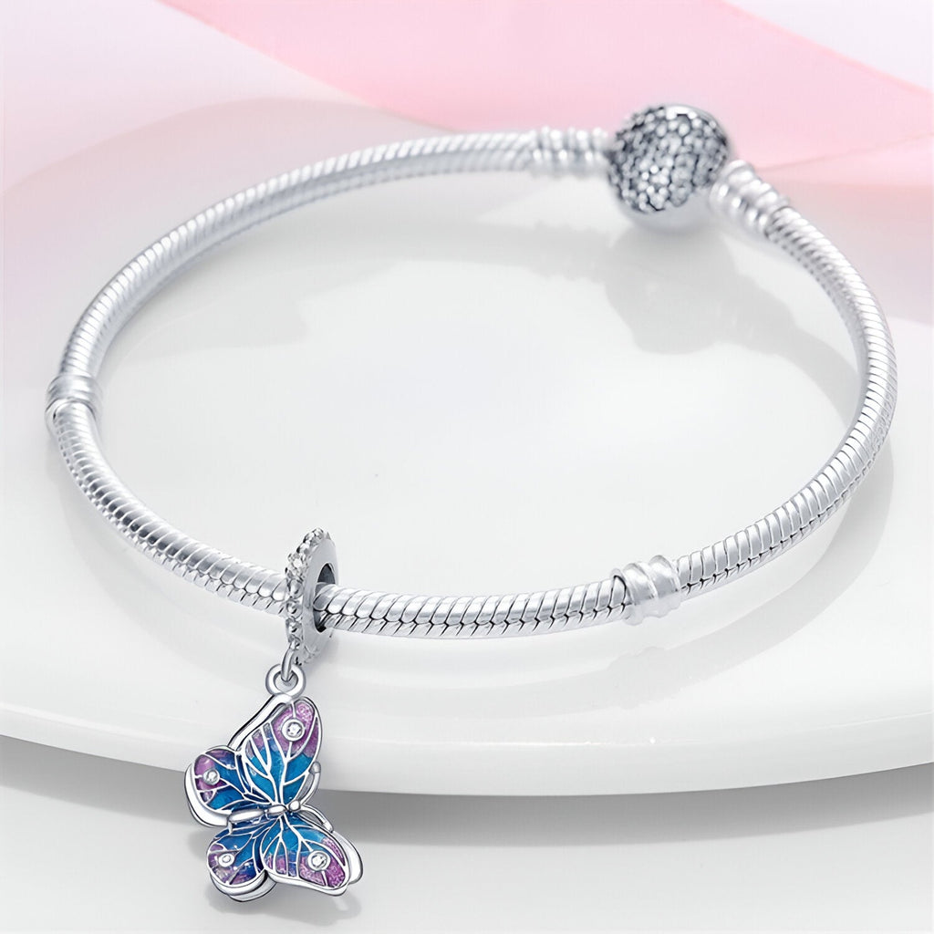 Bracelet en argent avec pendentif papillon bleu et rose aux détails gravés élégants.