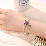 Bracelet blanc avec pendentif papillon orné de cristaux violets sur poignet féminin.