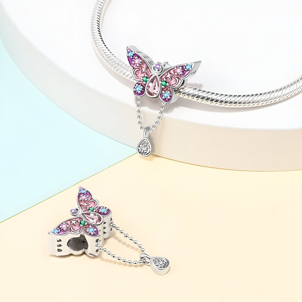 Pendentif papillon argenté orné de cristaux rose et bleu sur chaîne serpent brillante.