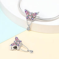 Pendentif papillon argenté orné de cristaux rose et bleu sur chaîne serpent brillante.