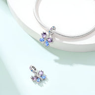 Pendentif papillon en métal argenté avec cristaux bleu et violet attaché à un bracelet serpent blanc.