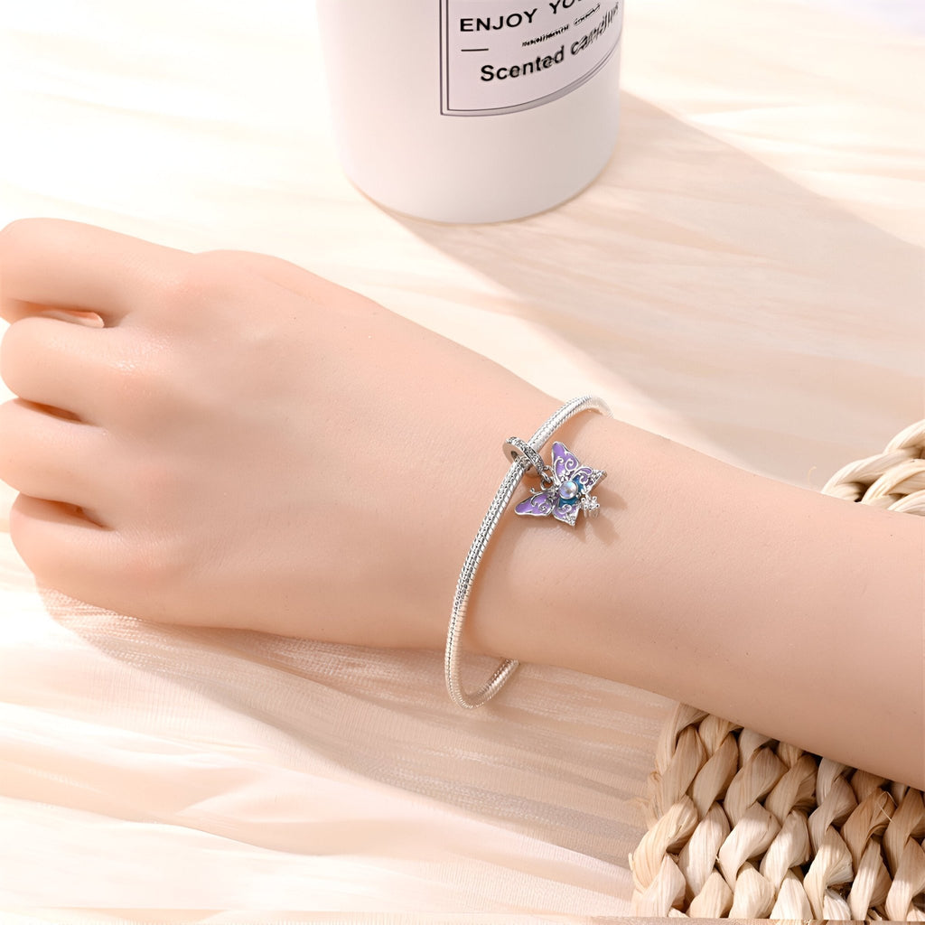 Bracelet argenté fin avec pendentif papillon bleu scintillant sur poignet féminin.
