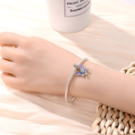 Bracelet argenté fin avec pendentif papillon bleu scintillant sur poignet féminin.