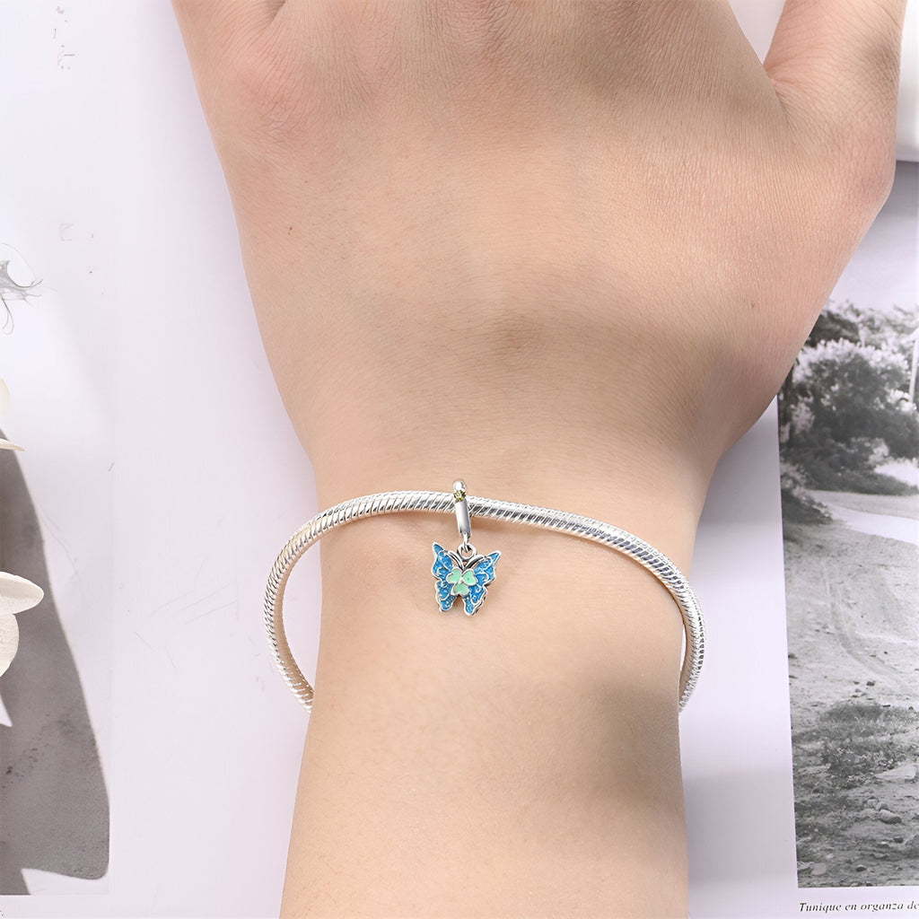 Bracelet argent avec pendentif papillon bleu délicat porté au poignet.