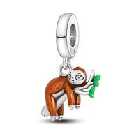 Pendentif charm paresseux marron accroché à une branche verte en métal argenté.