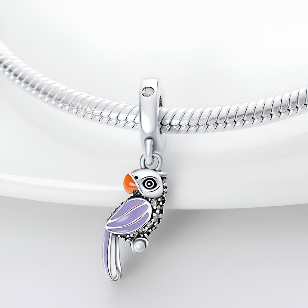 Pendentif perroquet en argent avec ailes violettes et bec orange sur chaîne serpent argentée.