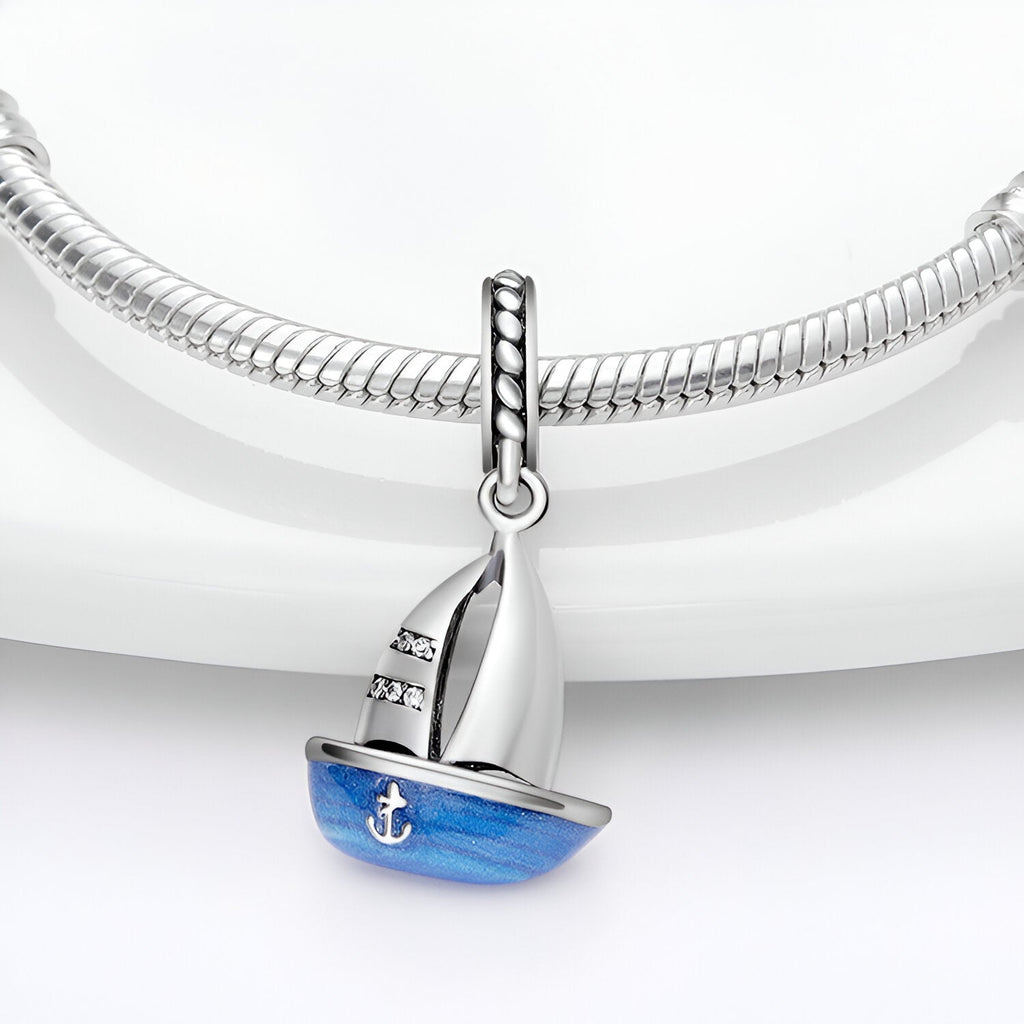 Charm pendentif petit bateau en argent avec voile blanche et coque bleue décorée d'une ancre blanche.