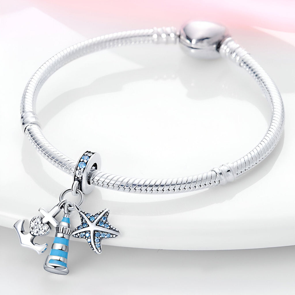 Bracelet en métal argenté avec pendentifs phare bleu, ancre et étoile de mer sertis de pierres bleues.