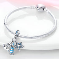 Bracelet en métal argenté avec pendentifs phare bleu, ancre et étoile de mer sertis de pierres bleues.