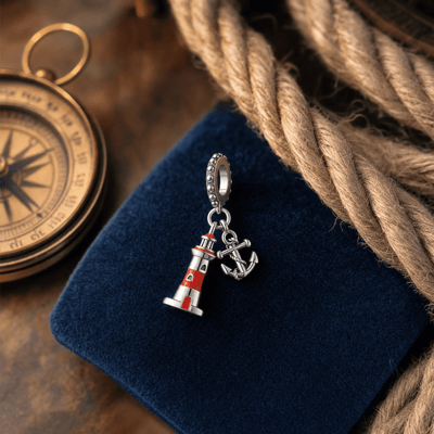 Charm pendant phare et ancre marine posé sur du velours bleu marine avec boussole et cordage nautique