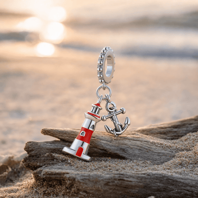 Charm pendant phare et ancre marine posé sur du bois flotté au bord de la mer au coucher du soleil