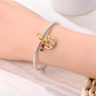 Bracelet argenté fin avec pendentif pinceau doré orné de pierres colorées scintillantes.