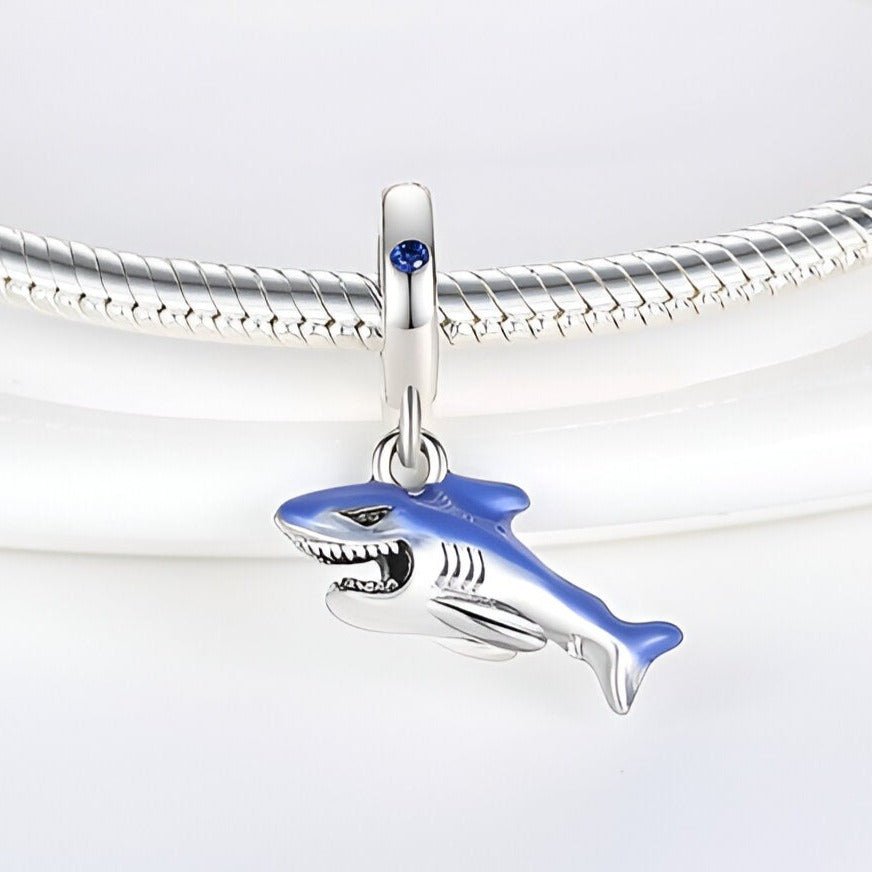 Charm pendentif requin en métal argenté avec détail bleu accroché à un bracelet serpent en argent.