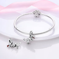 Bracelet argent avec pendentif T-Rex détaillé et fermoir en forme de fleur sur fond rose pâle.