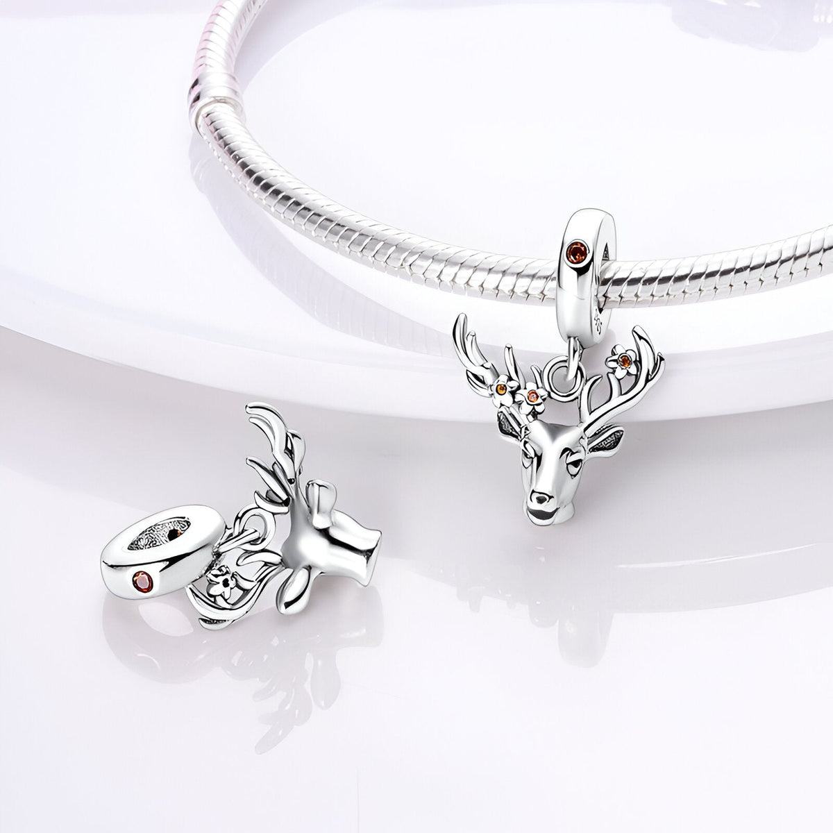 Charm pendentif tête de cerf en métal argenté avec détail pierre rouge, suspendu à un bracelet serpent.