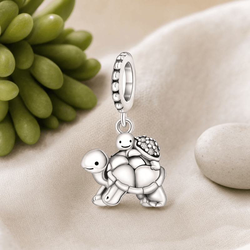 Charm pendentif tortues mère et enfant en argent posé sur tissu lin beige avec plante succulente et galet