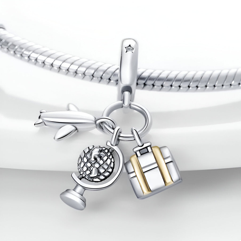 Charm pendentif en argent avec globe, avion et valise dorée, style voyage élégant.