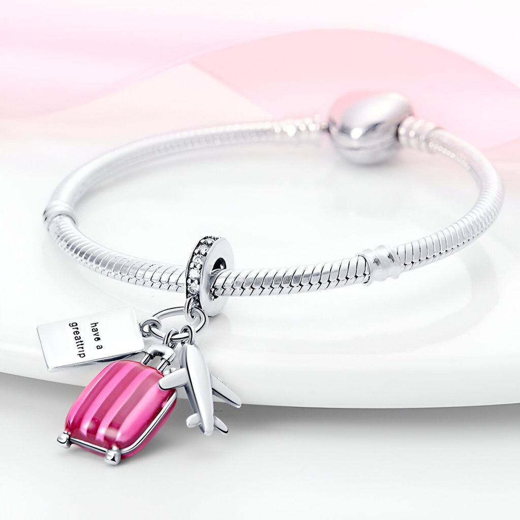 Bracelet argent fin avec pendentifs valise rose et avion argenté brillant.