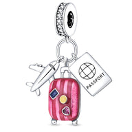 Charm pendentif argent avec valise rose, passeport blanc et avion argenté, détails couleurs vives.