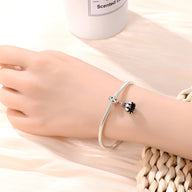 Bracelet argenté fin avec pendentif volant de badminton noir et blanc porté au poignet féminin.