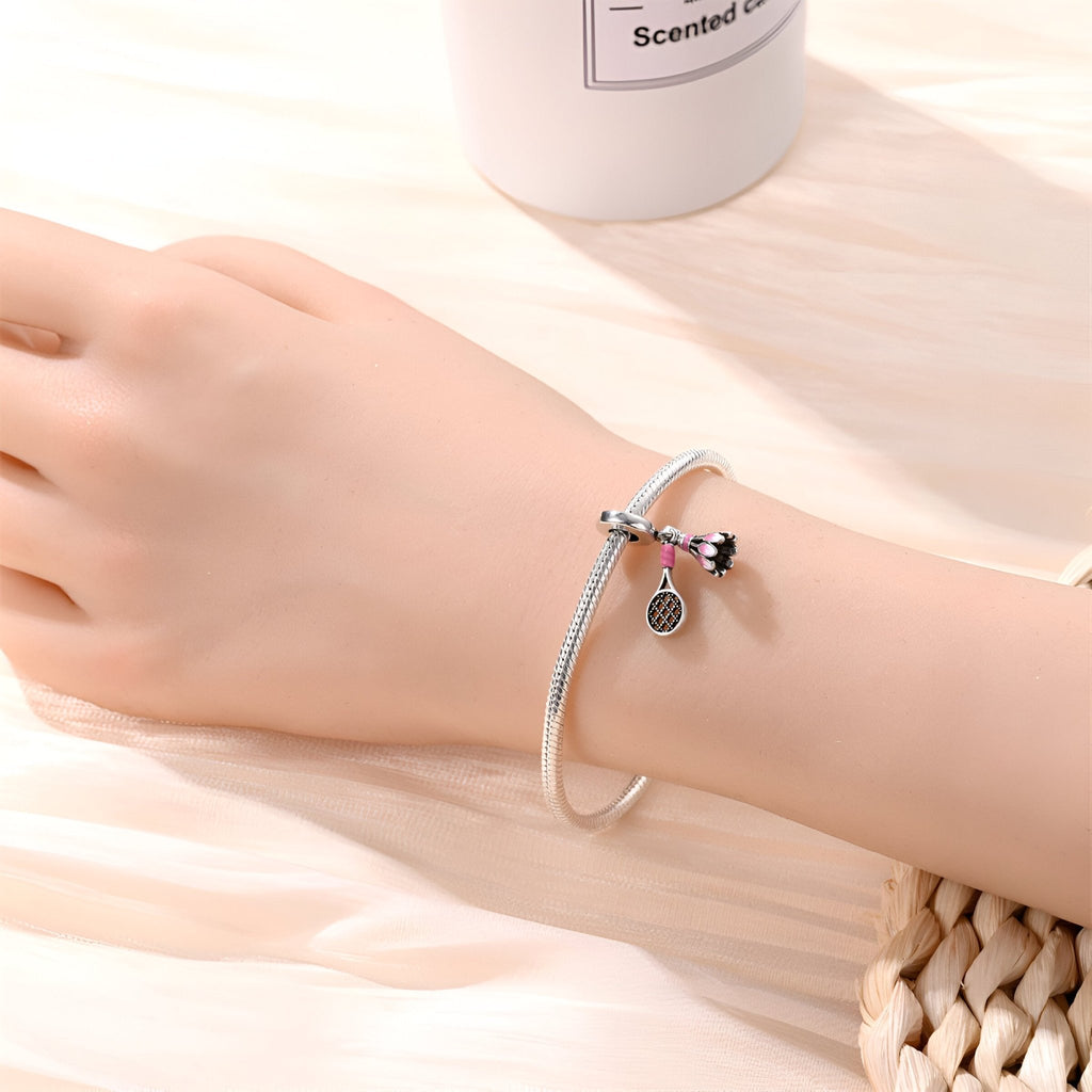 Bracelet argenté avec pendentifs volant de badminton et raquette, porté au poignet féminin.