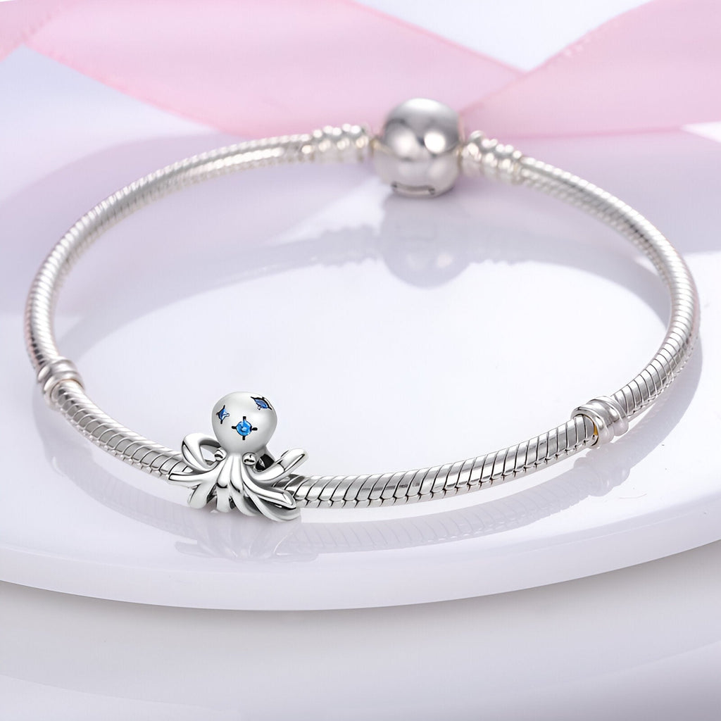 Bracelet argenté avec charm poulpe en argent orné d'étoiles bleues sur plaque blanche.