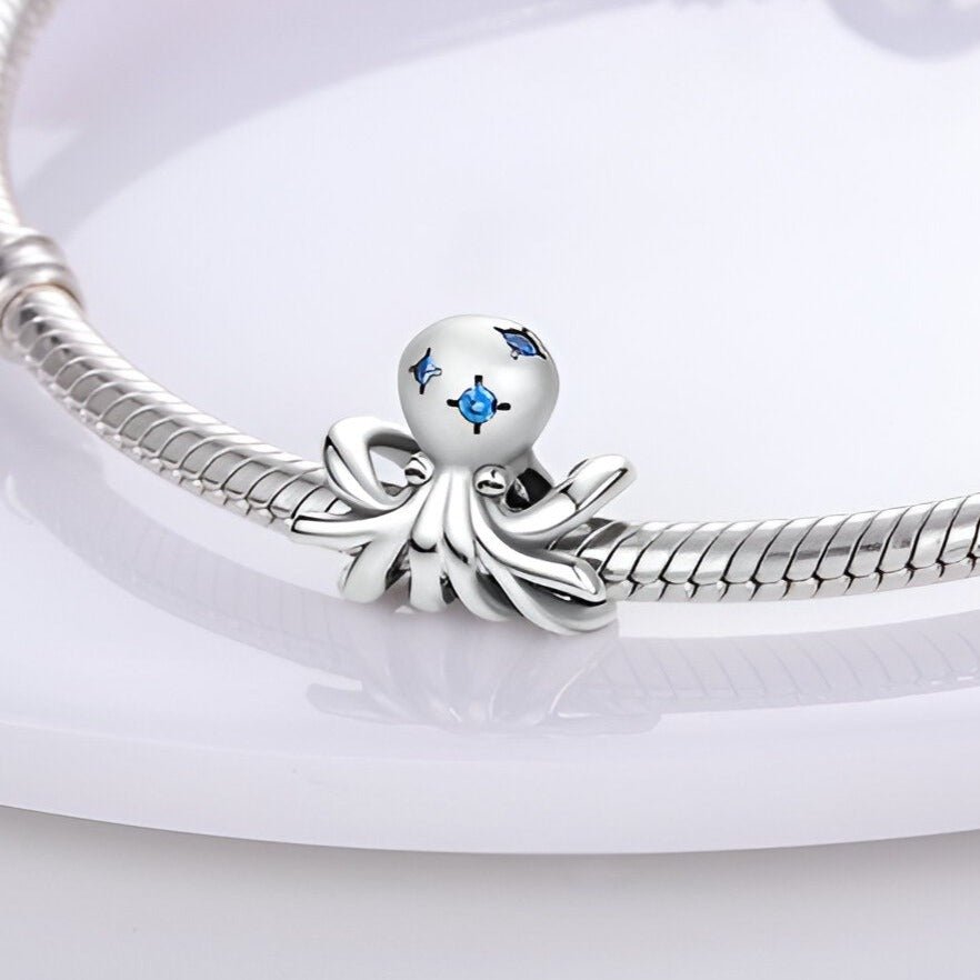 Charm poulpe en argent avec détails bleus, fixé sur un bracelet serpent argenté.