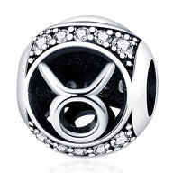 Charm rond en argent avec symbole Taureau noir et bordure ornée de petits cristaux blancs.