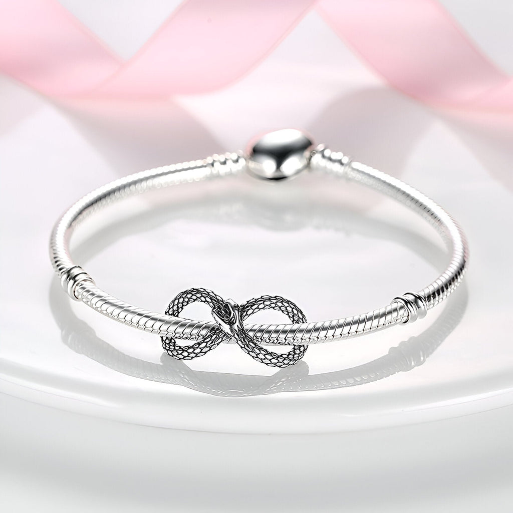 Bracelet rigide argent avec charm serpent infini texturé au centre.