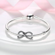 Bracelet rigide argent avec charm serpent infini texturé au centre.