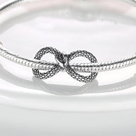 Charm serpent infini argenté avec détails d’écailles, monté sur bracelet serpent fin.