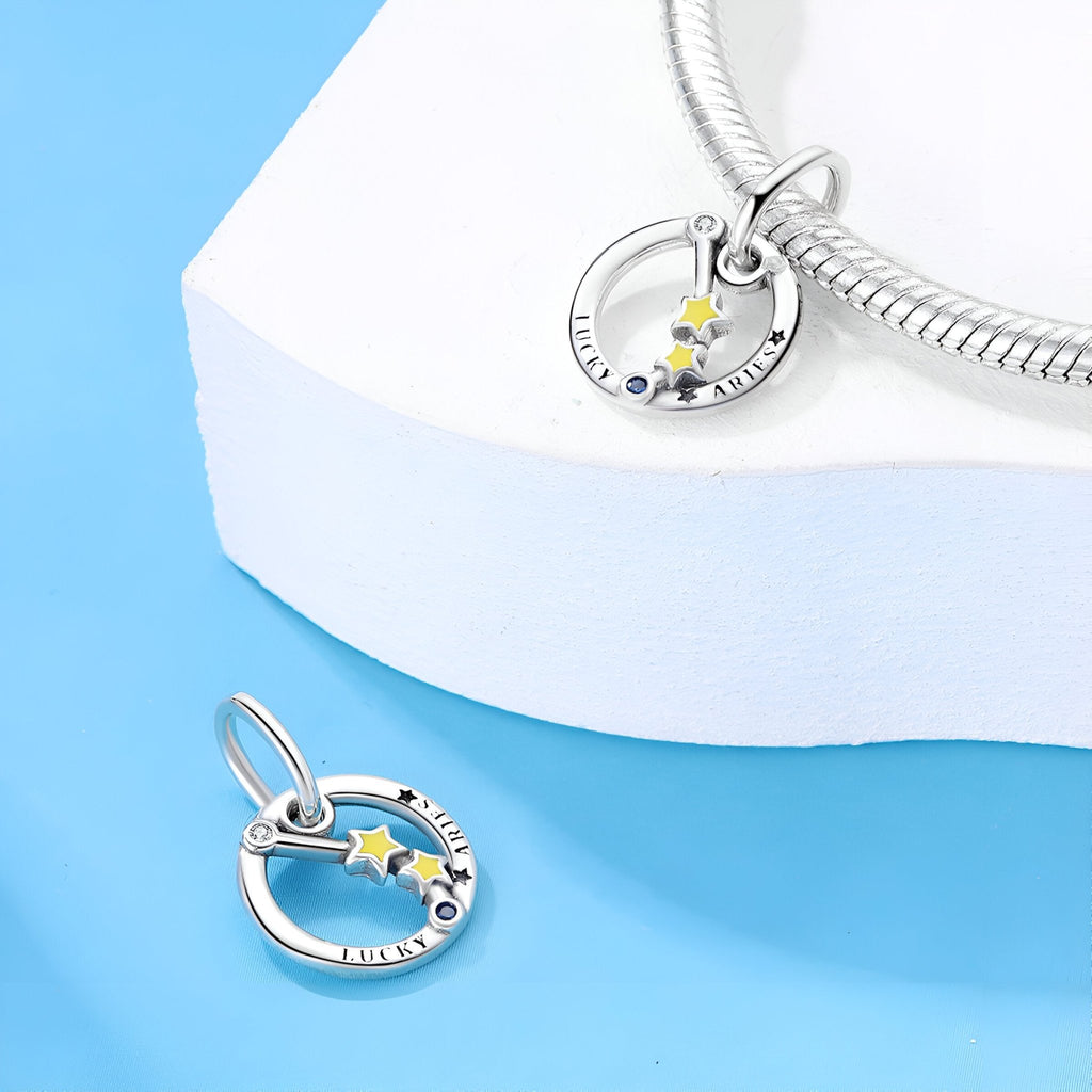 Charm en argent avec signe bélier, étoile jaune et pierres bleues sur cercle gravé.