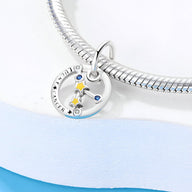 Charm argenté signe cancer avec étoiles colorées bleu, jaune et argent, suspendu à un bracelet serpent argenté.