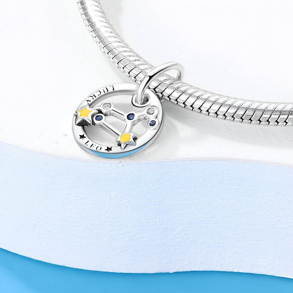 Charm rond en argent avec constellation lion et étoiles jaunes sur bracelet serpent argenté.