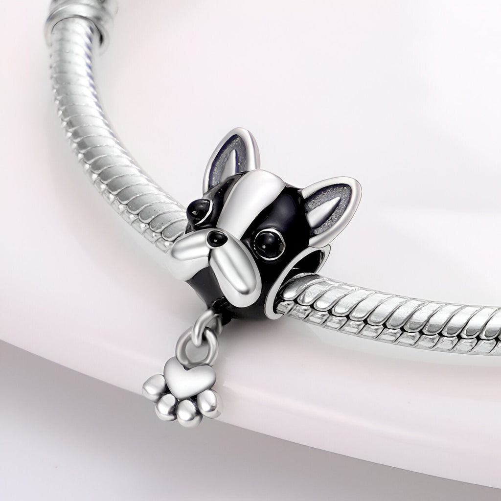 Charm argenté tête de bulldog français avec détails noirs et petite patte pendante sur bracelet serpent.