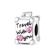 Charm valise en argent avec inscription "Travel with you" et deux cœurs roses scintillants.