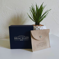 Coffret bleu marine avec logo blanc et pochette en tissu beige à bouton pression et logo embossé, plante verte en.