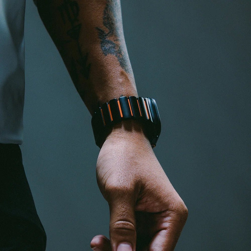 Bracelet Apple Watch robuste en titane noir mat avec finitions orange, lien articulé et fermoir sécurisé.