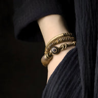 Duo de bracelets marron en bois, cuivre et agate, style mixte, porté au poignet avec tenue noire en laine côtelée.