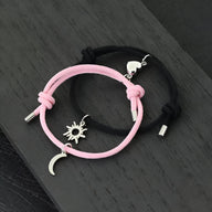 Duo de bracelets cordon rose et noir avec pendentifs soleil argenté et lune suspendus.