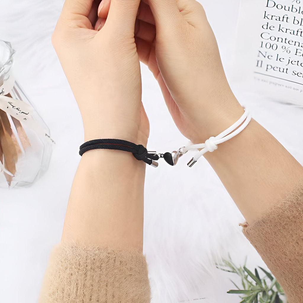 Duo de bracelets cordon noir et blanc avec cœurs aimantés sur poignets homme et femme.