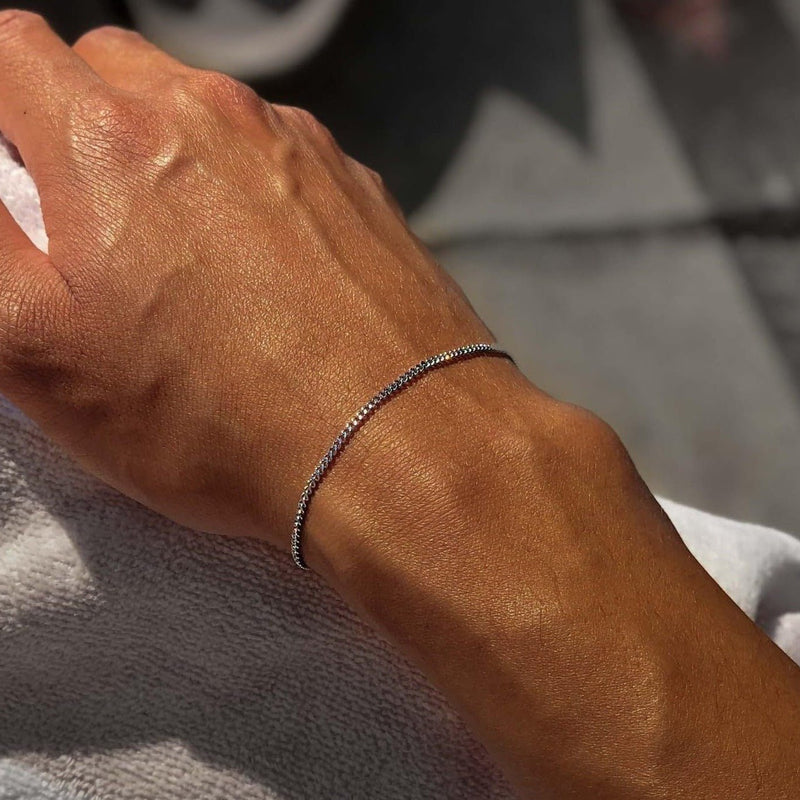 Bracelet jonc fin en acier inoxydable argenté porté au poignet masculin.