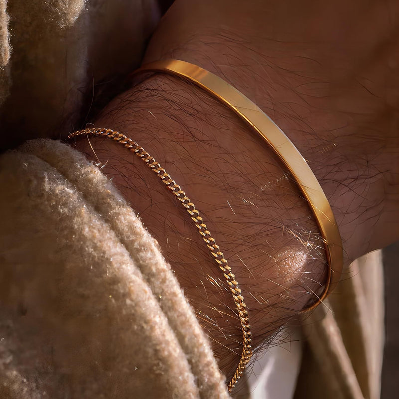 Duo de bracelets en acier inoxydable or, jonc lisse et chaîne fine maillée sur poignet masculin.