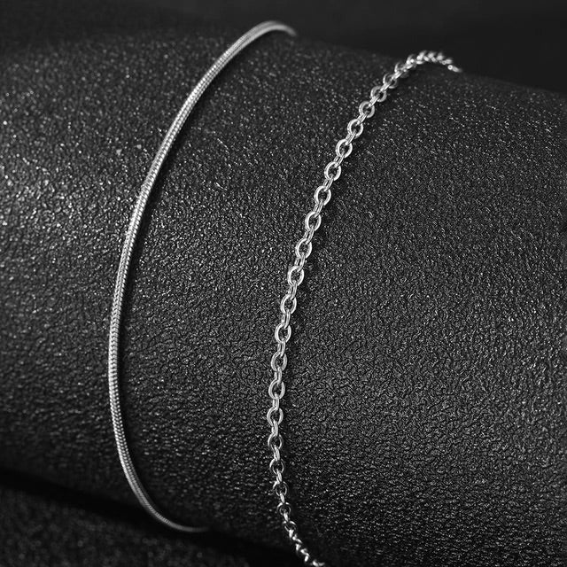 Duo de bracelets fins en acier inoxydable argenté, un lisse et un chaîne délicate.