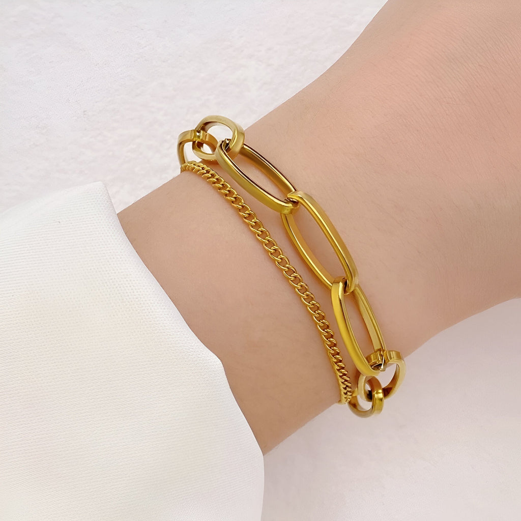 Duo de bracelets en acier inoxydable doré, avec maillons larges et chaîne fine élégante, porté au poignet féminin.