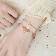 Duo de bracelets roses en pierres de cristal avec breloques étoile dorée et lune argentée attachés au poignet.