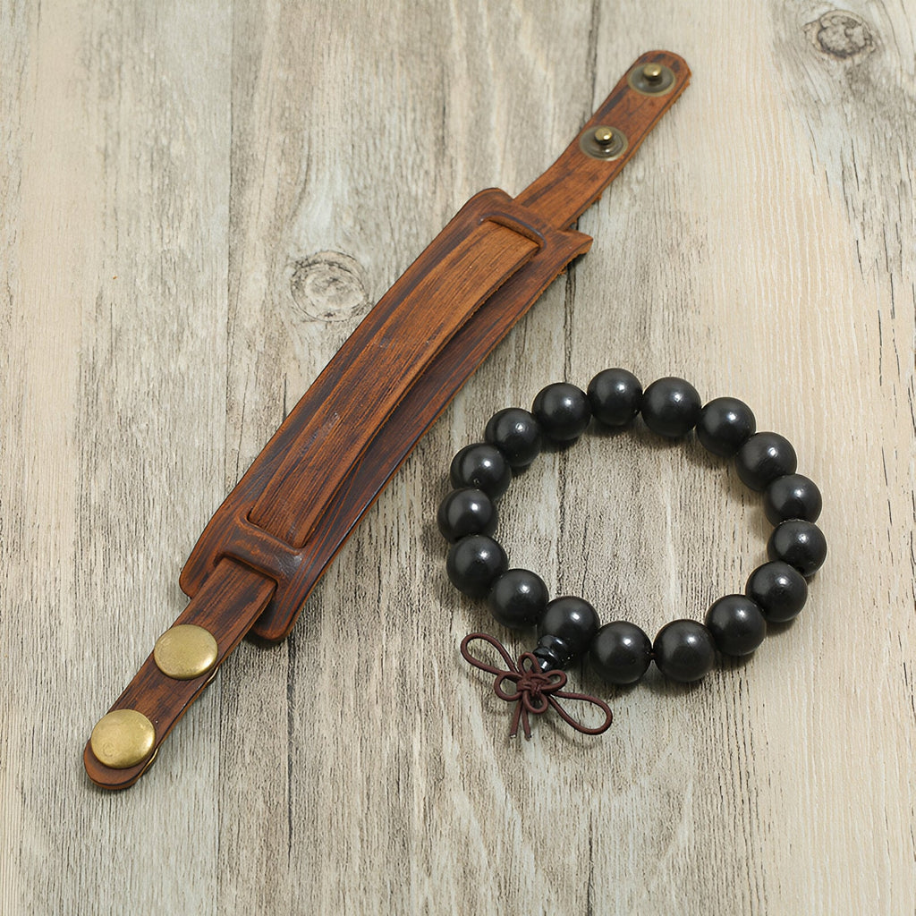 Duo de bracelets pour homme marron, un large en cuir avec fermeurs dorés et un en perles noires avec nœud décoratif rouge.