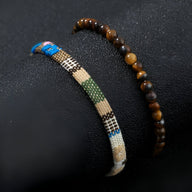 Duo de bracelets tibétains, un en pierres naturelles marron, l'autre en fil ciré beige, bleu et vert à motifs noirs.