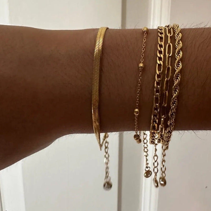 Ensemble de 5 bracelets fins en acier inoxydable doré avec chaînes variées et petits pendentifs, porté au poignet féminin.